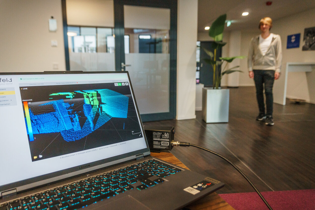 Mann steht vor einer Kamera, auf einem Laptop-Bildschirm sieht man die Aufnahme des Mannes vom 3D-Scanner.